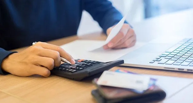 Person using a calculator while reviewing a receipt beside a laptop and wallet
