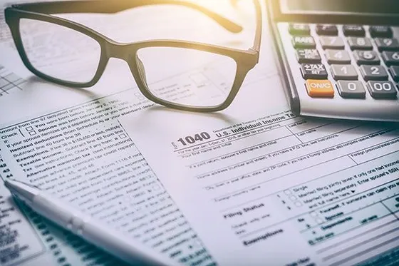 Eyeglasses, calculator, and pen on top of tax forms.