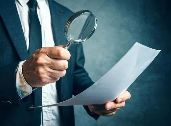 Man in suit examining a document with a magnifying glass, scrutinizing details.