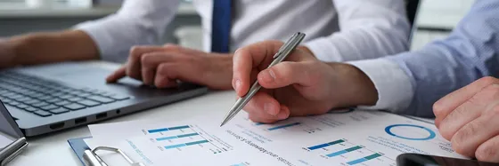 Two people reviewing financial charts with a laptop and pen.