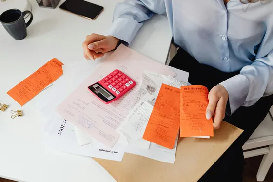 Person sitting at a desk surrounded by receipts and paperwork; using a calculator.