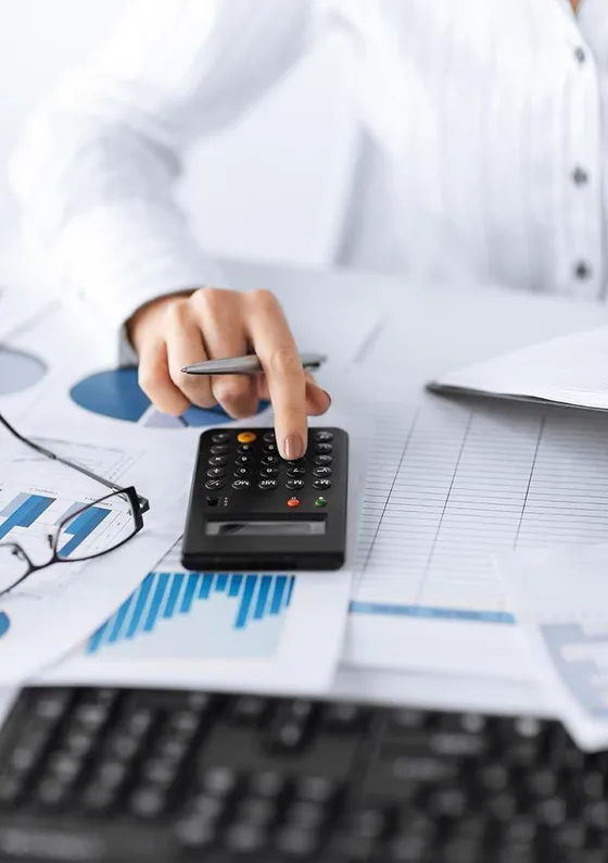 Person using calculator surrounded by financial reports, glasses, and keyboard.